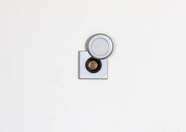 Kapı gözetleme deliği, sürgülü kapakla açıldı. Beyaz kapının üzerinde mercek var. Öteki dünyaya bir göz atma imkanı sunuyor.