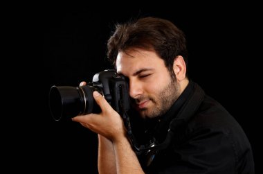 Genç fotoğrafçı profesyonel bir kamerayla çekim yapıyor. Stüdyoda dikkat çekici bir siyah arkaplan ile görüş açısına bakarken derinden konsantre oluyor.