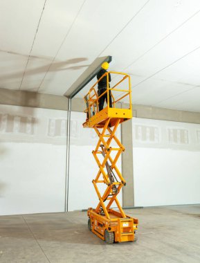 İnşaat işçisi güvenlik kaskı takıyor. Tadilat ya da inşaat çalışmaları sırasında depoya tavan kirişleri yerleştirmek için seyyar yükseltici çalışma platformu kullanıyor.