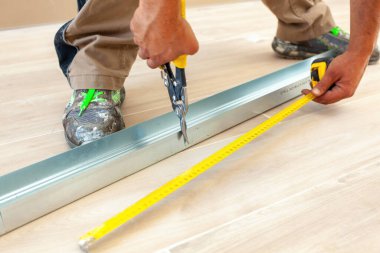 İnşaat işçisi, ev yenileme ve iyileştirme çalışmaları sırasında havacılık makaslarıyla metal bir profil çıkarıyor ve mezurayla ölçüm yapıyor