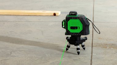 Bir ev yenileme projesi sırasında beton zemin üzerinde parlak bir çizgi yansıtan yeşil lazer düzeyi aracı, hassas ölçümler ve hizalama sağlama
