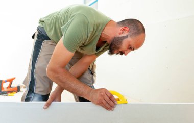 Konsantre inşaat işçisi ev yenileme sırasında zımpara makinesiyle alçıpanı zımparalıyor, düzleştiriyor, duvarda pürüzsüz bir son yaratıyor