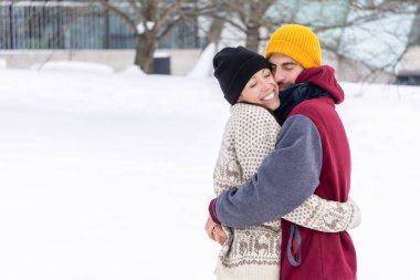 Kışın parkta kucaklaşan genç bir çift. Erkek ve kadın birbirlerine sarılıyorlar. Mutlu çift kışın dışarıda sarılıyor.