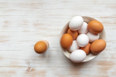 Kahverengi ve beyaz tavuk yumurtalı tabak ve bir tane de ahşap masada. Kasede organik yumurta var. Tahta arka planda kahverengi yumurtalar. Doğal sağlıklı gıda konsepti. Üst görünüm, düz görünüm, kopyalama alanı.