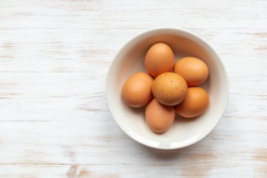 Tahta masanın üzerinde kahverengi tavuk yumurtası tabağı. Tahta arka planda kahverengi yumurtalar. Kasede organik yumurta var. Doğal sağlıklı gıda konsepti. Üst görünüm, düz görünüm, kopyalama alanı.