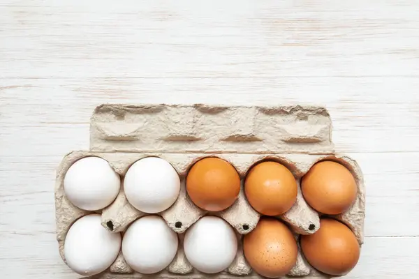 Brown and white eggs in open carton box. Fresh organic chicken eggs in carton pack on wooden surface. Top view with copy space. Natural healthy food and organic farming concept.