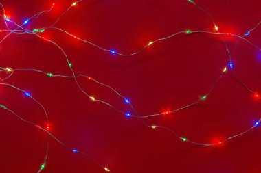 Yılbaşı süslemeleri olan metin için arka plan. Kırmızı arka planda küçük ışıklı bir çelenk. Parlayan Noel çelengi. Noel ve Yeni Yıl 'ın sembolü olarak festival ışıkları. Tasarım için arkaplan.