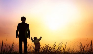 Silhouette of father and son standing on grass  against sunset sky background