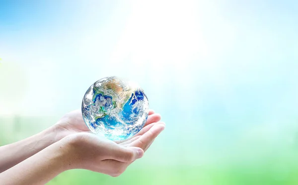 Human hands holding earth globe over blurred nature background. Elements of this image furnished by NASA