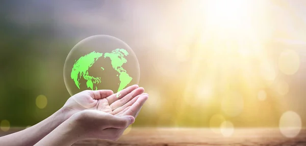 Earth day concept, A green earth globe in human hands over blurred beautiful nature background