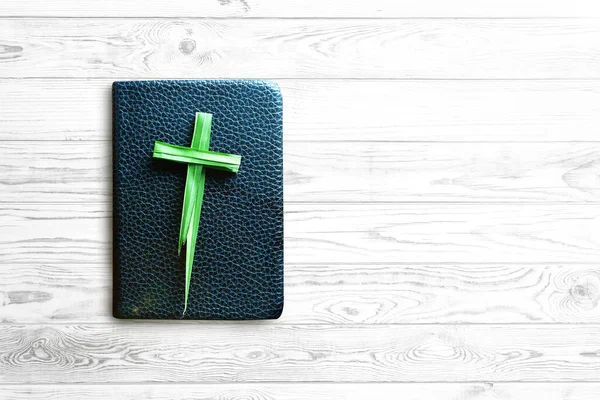 Palm Sunday concept, cross made of palm leaves on black bible on white wooden table