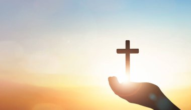 human hand holding the Jesus Christ cross on sunset sky background. clipart