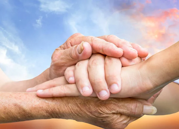 Old and young holding hands on sunrise sky background,