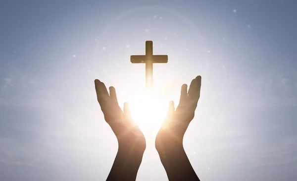 Brightly shining sunlight and Silhouette of cross in human hand