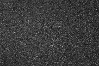 Arka planda düz olmayan bir yüzeyi olan siyah bir beton duvar var..