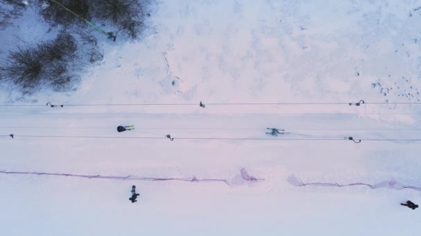 スキーリフトエレベーターの空中トップビュー スキー場の雪の斜面にはスキーヤーやスノーボーダーが登ります 冬の霜の日の雪の斜面でのスキードラッグリフトの仕事 オーバーヘッドビュードローン静的ショット — ストック動画