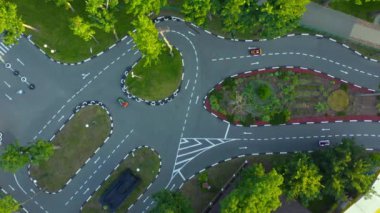 Karting Attraction Track: İnsanlar asfalt yarış pistinde küçük arabalara biniyor: havadan görüntülü insansız hava aracı. Beyaz işaretli asfalt yolda karting hareketi.