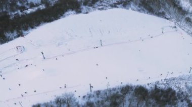 Kayakçılar ve snowboardcularla karla kaplı bir kayak pisti. İnsanlar karda kayak ve snowboard yapıyor. Hava aracı görüntüsü. İnsanlar soğuk kış havasında yamaçta kayak yapıyorlar. Hava aracı çekimi..