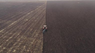 Traktör tarlada sabanla çalışıyor. Traktör verimli kara toprağı sürüyor. Hava aracı takibi görüntüsü. Bahar hazırlayıcı tarım işi. Bereketli Chernozem toprağının yetiştirilmesi.