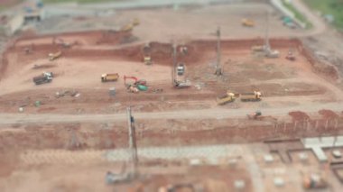 Bir sürü inşaat malzemesi olan büyük bir inşaat. Kil büyüklüğünde bir çukurda inşaat malzemeleri. İnşaat alanında kamyonlar, vinçler ve kazıcılar çalışıyor. Eğim değiştirme efekti.