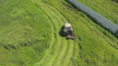 Eski traktör yeşil olgun çimleri çayırda biçer. Hava aracı görüntüsü. Summer Haymaking traktör çim biçme makinesiyle. Traktör saman kurutmak için yeşil çim biçer - üst hava görüntüsü. 