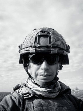 Powerful portrait of a 37-year-old Ukrainian military soldier in full body armor, ballistic helmet, and protective goggles, staring straight into the camera with a calm and focused expression.