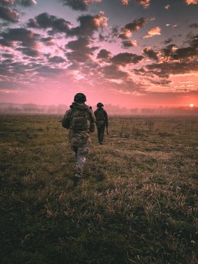 Two soldiers in camouflage and armed to the teeth set out on a mission towards the East in the pre-dawn light before the sun rises. Tactical movement of two special-purpose fighters around the area.