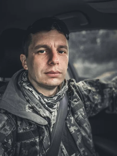 Portrait of a tired soldier of the Ukrainian army in camouflage. A 37-year-old man sits in a car. The consequences of post-traumatic war syndrome - lack of joy.