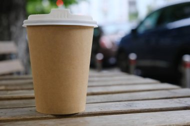 Beyaz plastik kapaklı kağıt kahve fincanı. Yol kenarındaki masada kahverengi kağıt kahve fincanı, kopyalama alanı. Kağıt kahve fincanındaki yazının şablonu.
