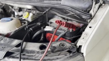 Arka planda tampon, jant ve lastik gibi otomotiv parçalarını gösteren aküye bağlı bir araba motorunun ayrıntılı fotoğrafı