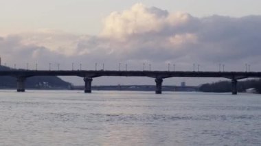 Gölün üzerinde uzanan bir kiriş köprüsü, suya yansıyan bulutlu gökyüzü. Uzakta kaybolan ufuk sakin ve resimsel bir manzara yaratır.