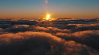 Güneş, gün batımında gökyüzündeki bulutların arasından sıcak bir parıltı yayıyor. Atmosferde güzel bir parlama yaratıyor.