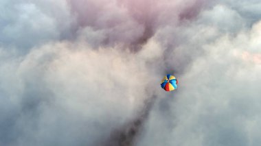 Renkli paraşüt kümülüs bulutları arasında süzülüyor. Mavi gökyüzünde, rüzgar tarafından sürüklenen büyüleyici bir meteorolojik fenomen.