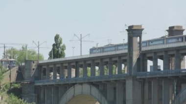 Güneşli bir günde arka planda, Viyadük üzerinde seyahat eden bir tren. Arka planda şehir olan iki katlı bir köprüden bir tren yavaşça geçiyor..