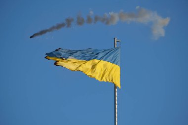 Açık mavi gökyüzünde dalgalanan parçalanmış Ukrayna bayrağı aşınma ve hasar izleri ile dayanıklılık ve dayanıklılığı simgeliyor..