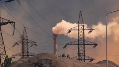A power plant with large transmission towers and smoke billowing from a smokestack. The industrial scene, with power lines and a hazy sky, emphasizes energy productions environmental impact