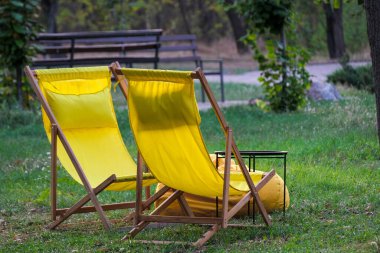 İki canlı sarı iskemle yemyeşil çimenlere yerleştirilir ki bu da açık havada rahatlamak için birebirdir.