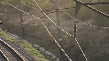 Gün batımının yumuşak ışığıyla güzelce aydınlatılan tren raylarının ve elektrik hatlarının huzurlu ve huzurlu manzarası.