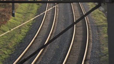 Yeşilliklerle çevrili kıvrımlı tren raylarının büyüleyici bir fotoğrafı, çizgileri ve dokuları vurguluyor.