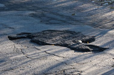 Bu resim, yol bakımı çalışmalarında karşılaşılan zorlukları vurgulayan ve yüzeydeki görünür çatlaklarla işaretlenmiş bir asfalt yamasını gösteren bir yol bölümünü içeriyor.