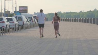 Çarpıcı bir sabah, iki koşucu, aktif ve sağlıklı bir yaşam tarzına örnek olarak, geniş bir rıhtım boyunca egzersiz yapıyor: Ağustos 2024 - Kyiv, Ukrayna