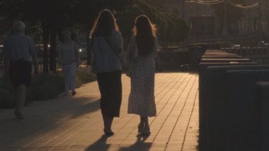 İki yakın arkadaş, sakin bir şehir atmosferiyle çevrili güzel bir yürüyüş yolu boyunca gün batımında yan yana yürümenin keyfini çıkarıyorlar - Ağustos 2024: Kyiv, Ukrayna