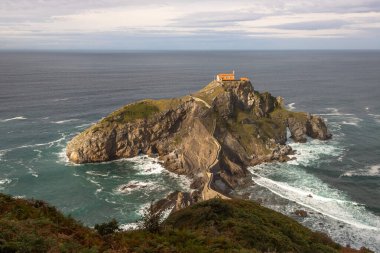 San Juan de Gaztelugatxe adası ve kıyı kasabaları Bakio ve Bermeo arasında yer alan inziva yerinin kıyıya taş bir köprü ve 241 basamaklı bir merdiven, İspanya 'nın Bask sahili,.