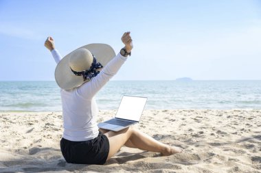 Herhangi bir konsept üzerinde çalış. Sahilde bilgisayarla çalışan genç bir kadının arka görüntüsü.