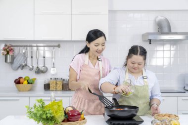 Anne ve kızı mutfakta mutlu bir şekilde yemek pişiriyor.