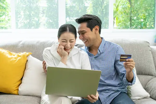 Happy Asian couple use credit card for online shopping at home