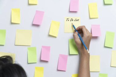 Bir not kağıdına bir şeyler yazan ve duvara yapıştıran genç bir kadın.