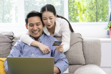 Evde online alışveriş yapmak için kredi kartı kullanan mutlu bir çift..