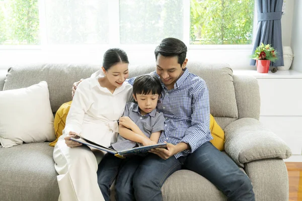 The parents and child read a book together in the living room