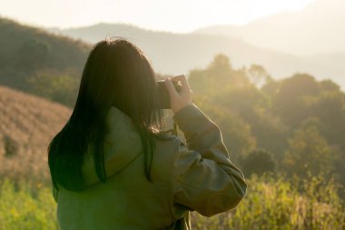 Bir kadın kamp gezisi sırasında dağ zirvesinde gün batımının fotoğraflarını çekiyor.